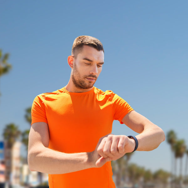Man in orange shirt checking his watch against a blue sky and palm tree background