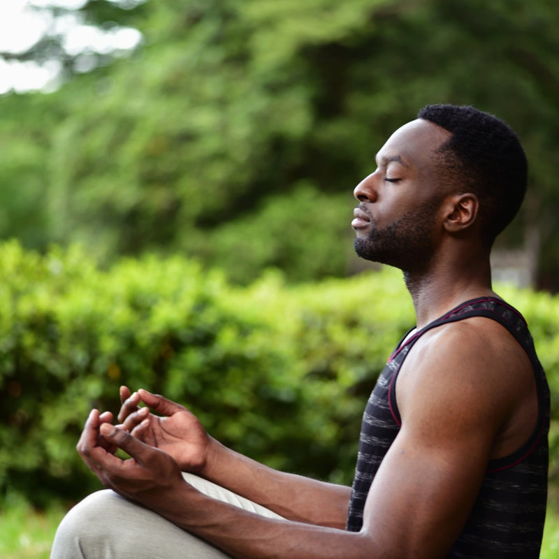 Man meditating outdoors with greenery in the background
