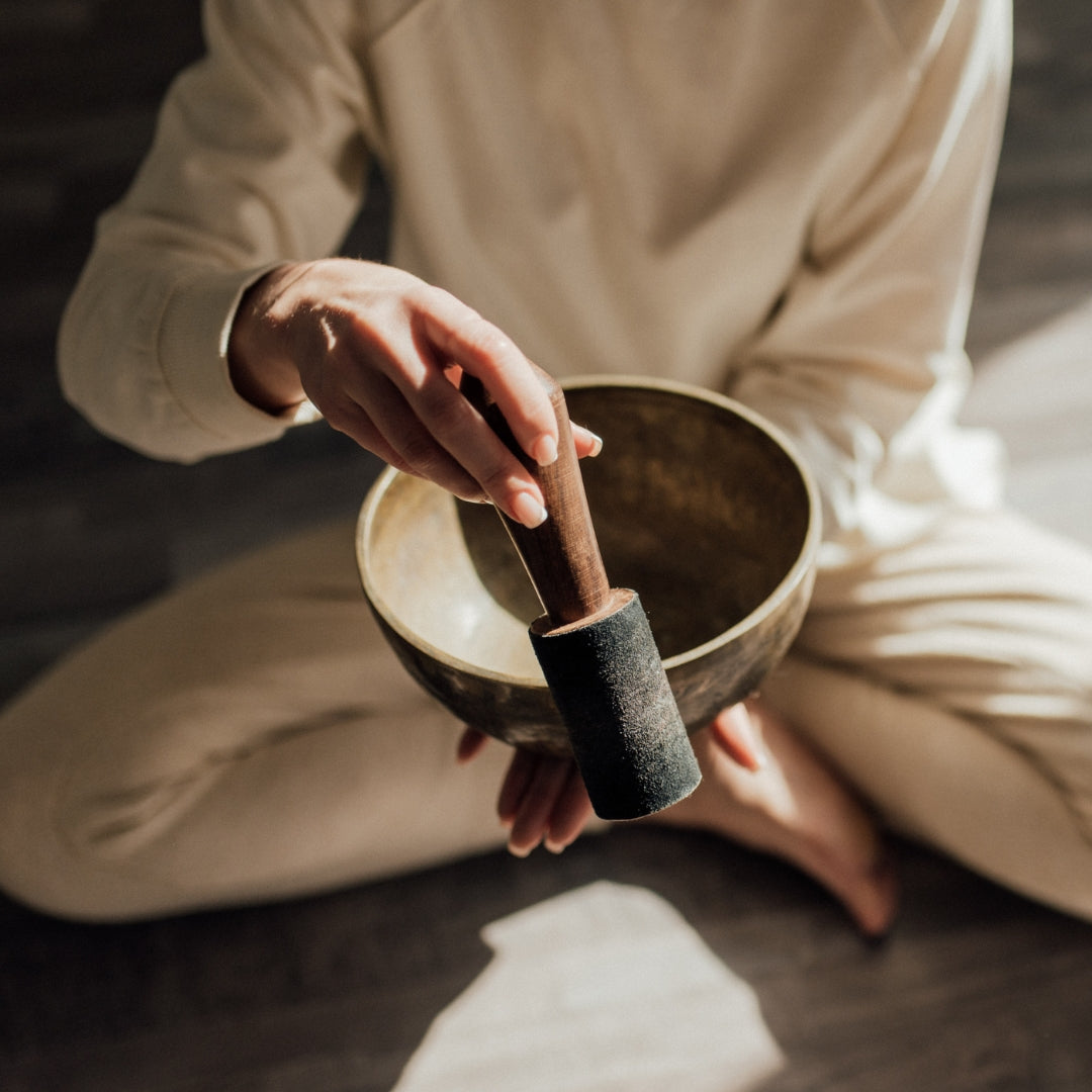 Person holding a wooden singing bowl with a mallet in a serene setting