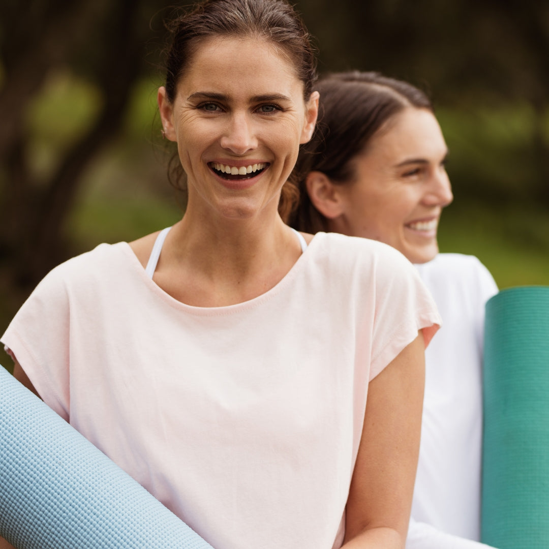 Two women with yoga mats, smiling outdoors